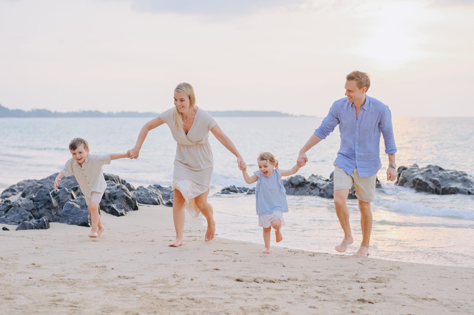 Family running on a rocky beach at sunset in Khao Lak